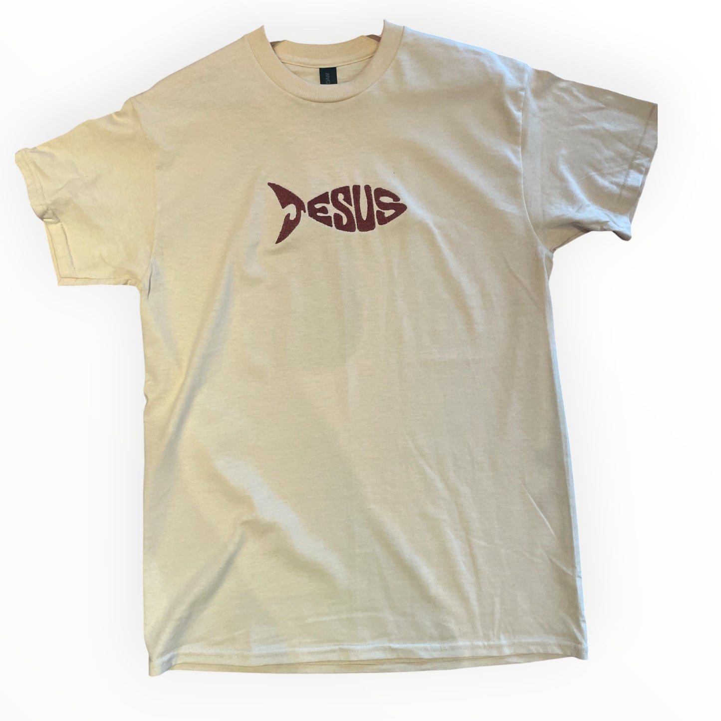 Jesus fish, Christian T-shirt, beige color with bronze embroidered text laying flat on wooden background