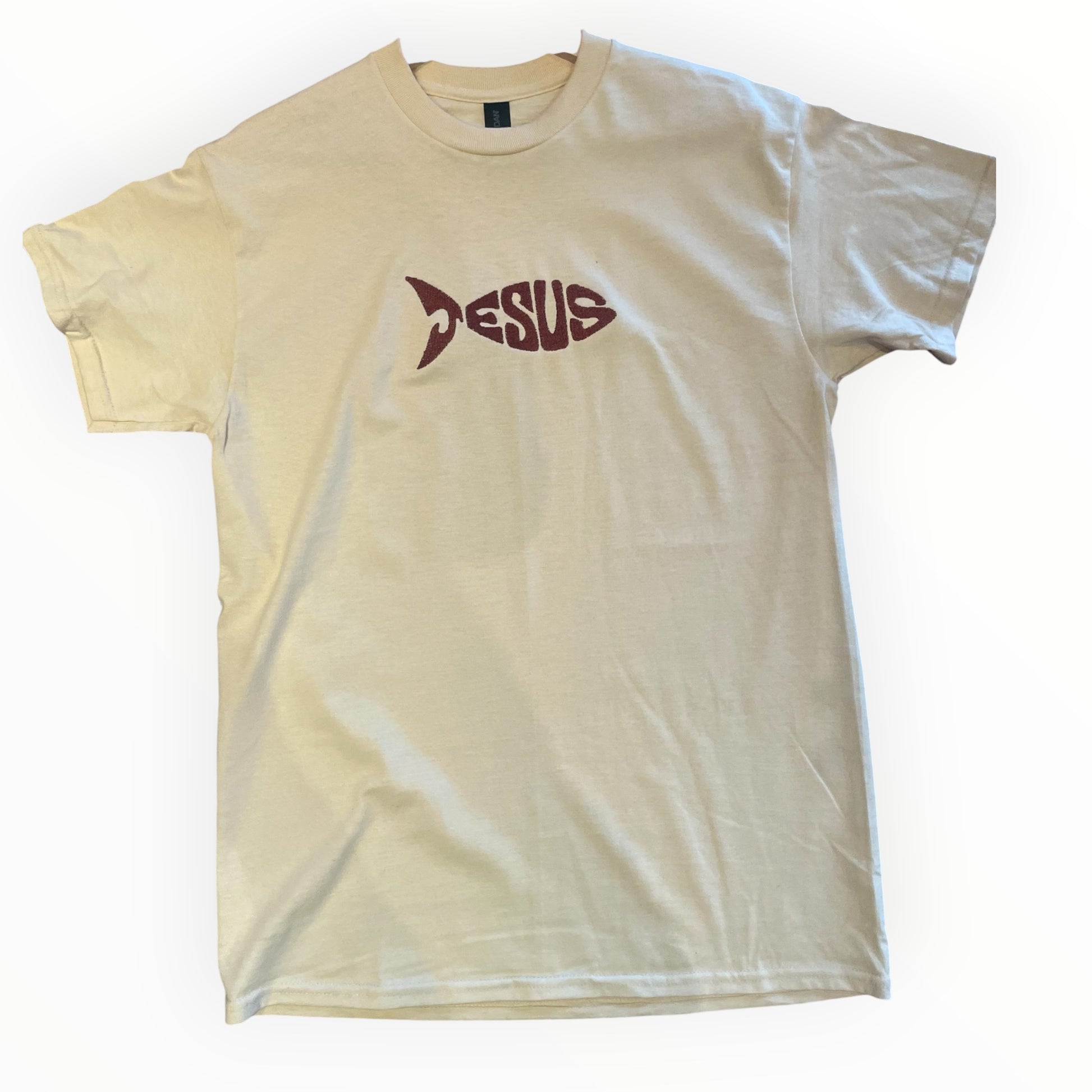 Jesus fish, Christian T-shirt, beige color with bronze embroidered text laying flat on wooden background